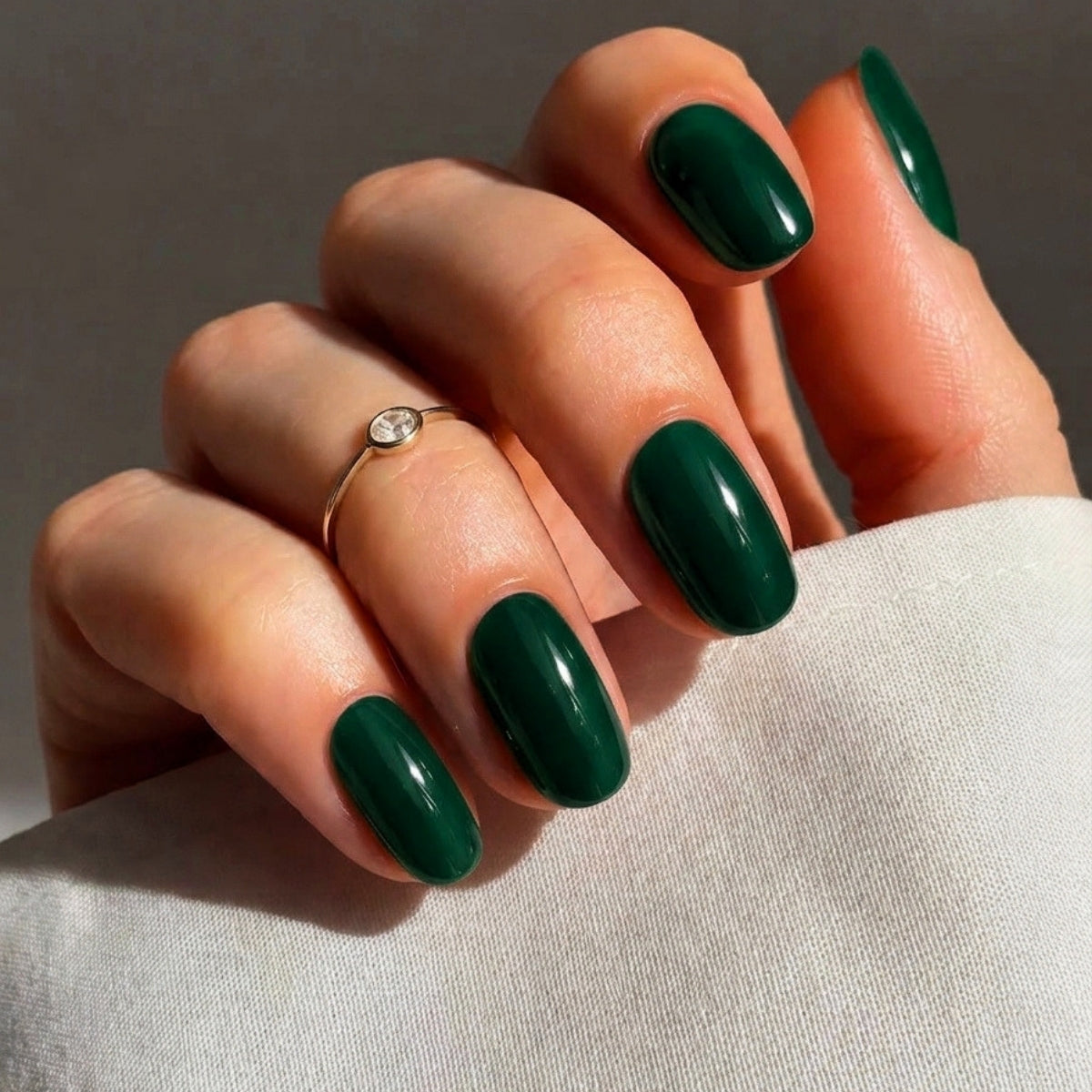 Hand mit dukelgruenen Naegeln mit schlichtem grauen Hintergrund und weisser Bluse.